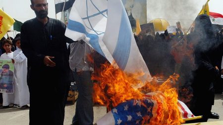 BAGHDAD, IRAQ - JULY 31:  An Iraqi man burns Israeli and American flags as Iraqi women take part in a protest against Israel's attacks on civilians in Lebanon on July 31, 2006 in the Sadr Shiite city in Baghdad, Iraq. In the deadliest Israeli attack since hostilities began, more than 50 people were killed in Qana yesterday, many of them children, when the house they were sheltering in was bombed by Israeli war planes.  (Photo by Wathiq Khuzaie/Getty Images)